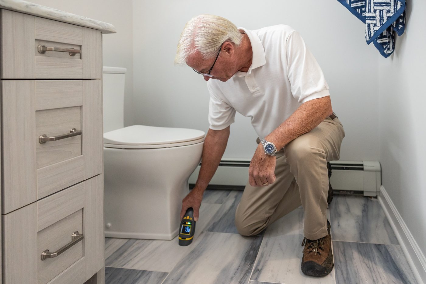 Man kneeling beside a toilet checking the floor and pipework with a handheld device